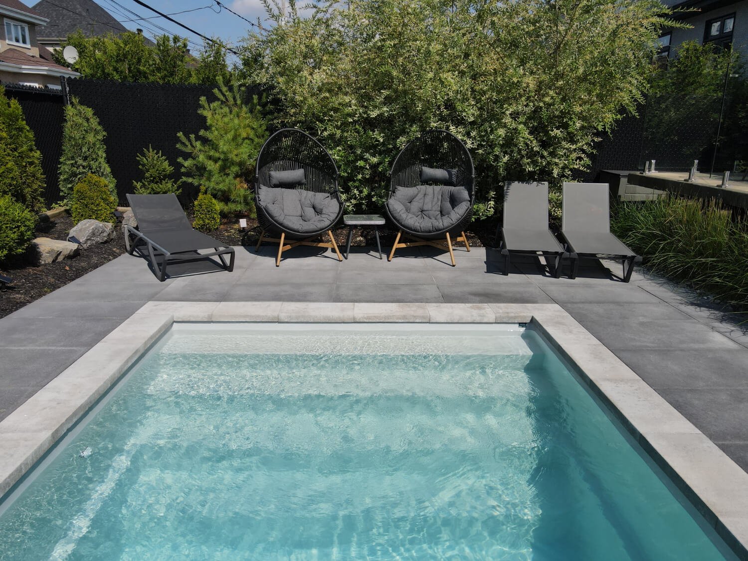 Fiberglass inground pool with lounge area, egg chairs and sun loungers