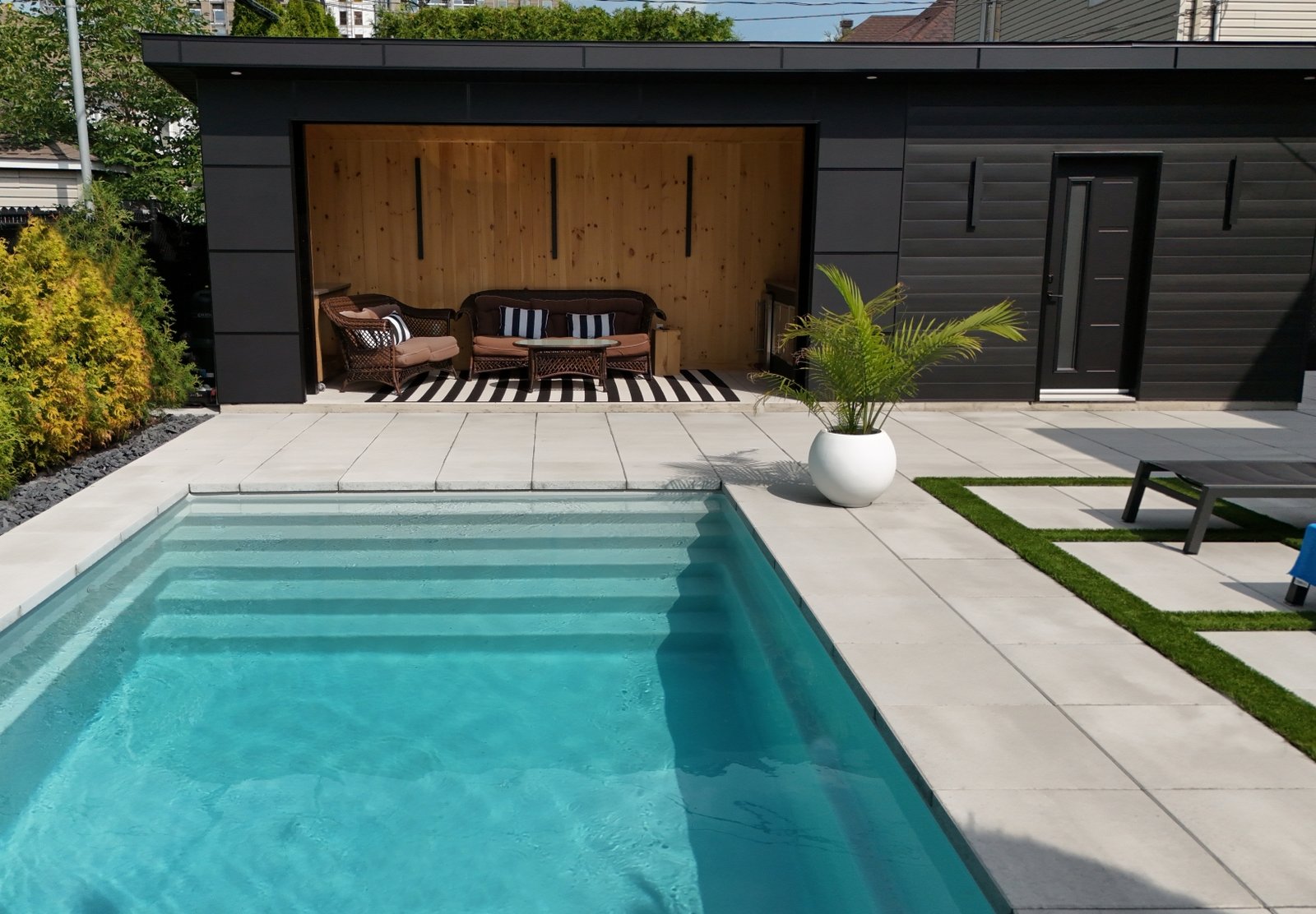 Modern inground pool with black pool house, wood outdoor lounge and stone patio
