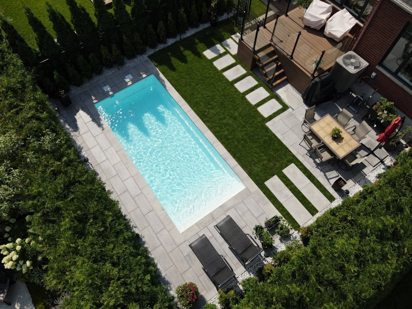 Aerial view of a long inground pool with lawn, lounge chairs and stone patio