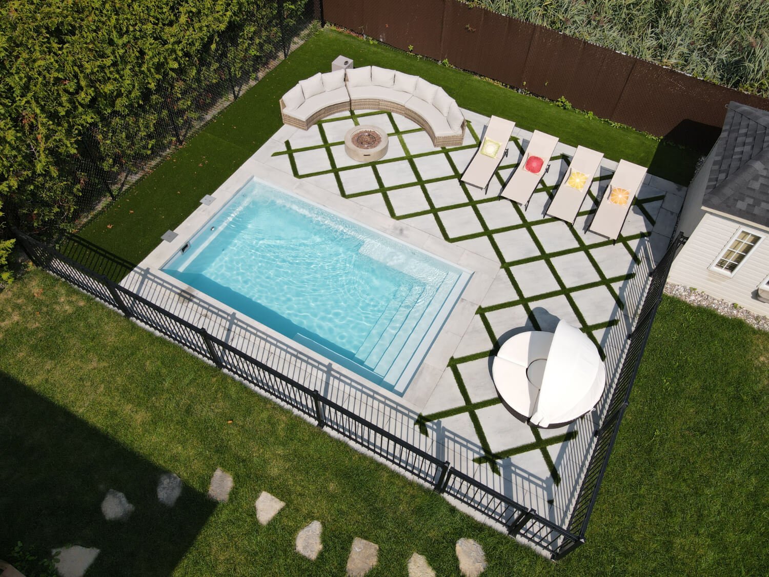 Aerial view of a fiberglass inground pool with pavers, outdoor lounge and synthetic turf