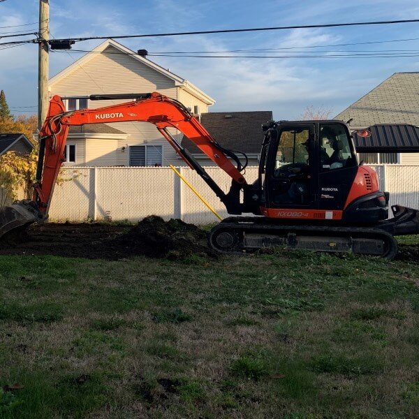 Excavatrice rouge Kubota effectuant les travaux de terrassement pour l'installation d'une piscine creusée