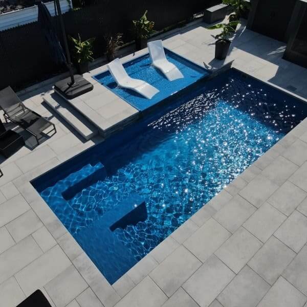 Piscine rectangulaire avec terrasse en béton blanc, chaises longues blanches, spa intégré, aménagement paysager minimaliste