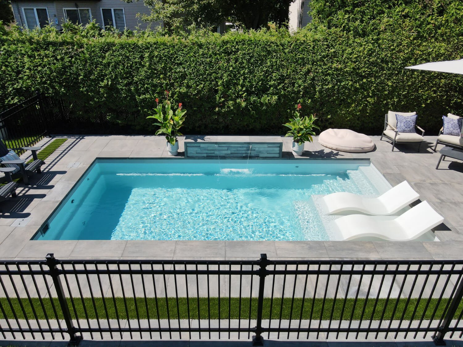 Turquoise fiberglass inground pool with lounge chairs and cedar hedge in Quebec