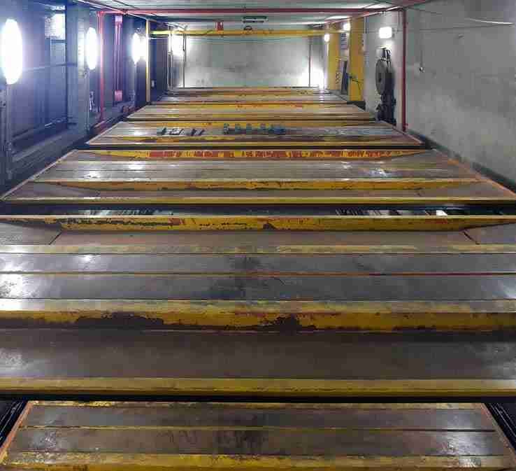 Intérieur du parking automatique avant rénovation - plateformes jaunes et rouges rouillées, murs sales, éclairage insuffisant