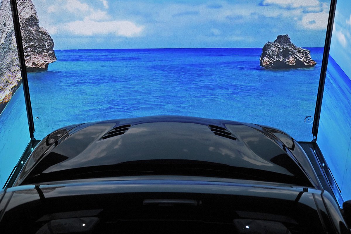 Auto nera vista dall'interno con tetto panoramico aperto, vista sul mare blu con rocce e cielo azzurro