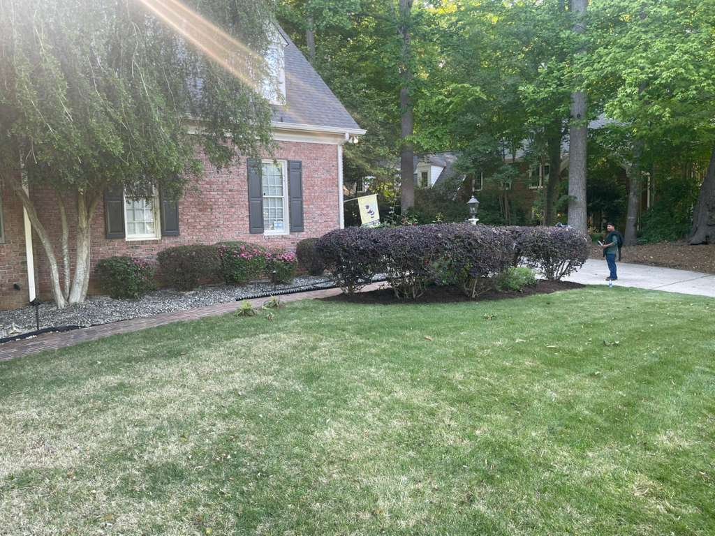 Brick home with well-pruned shrubs and mature trees