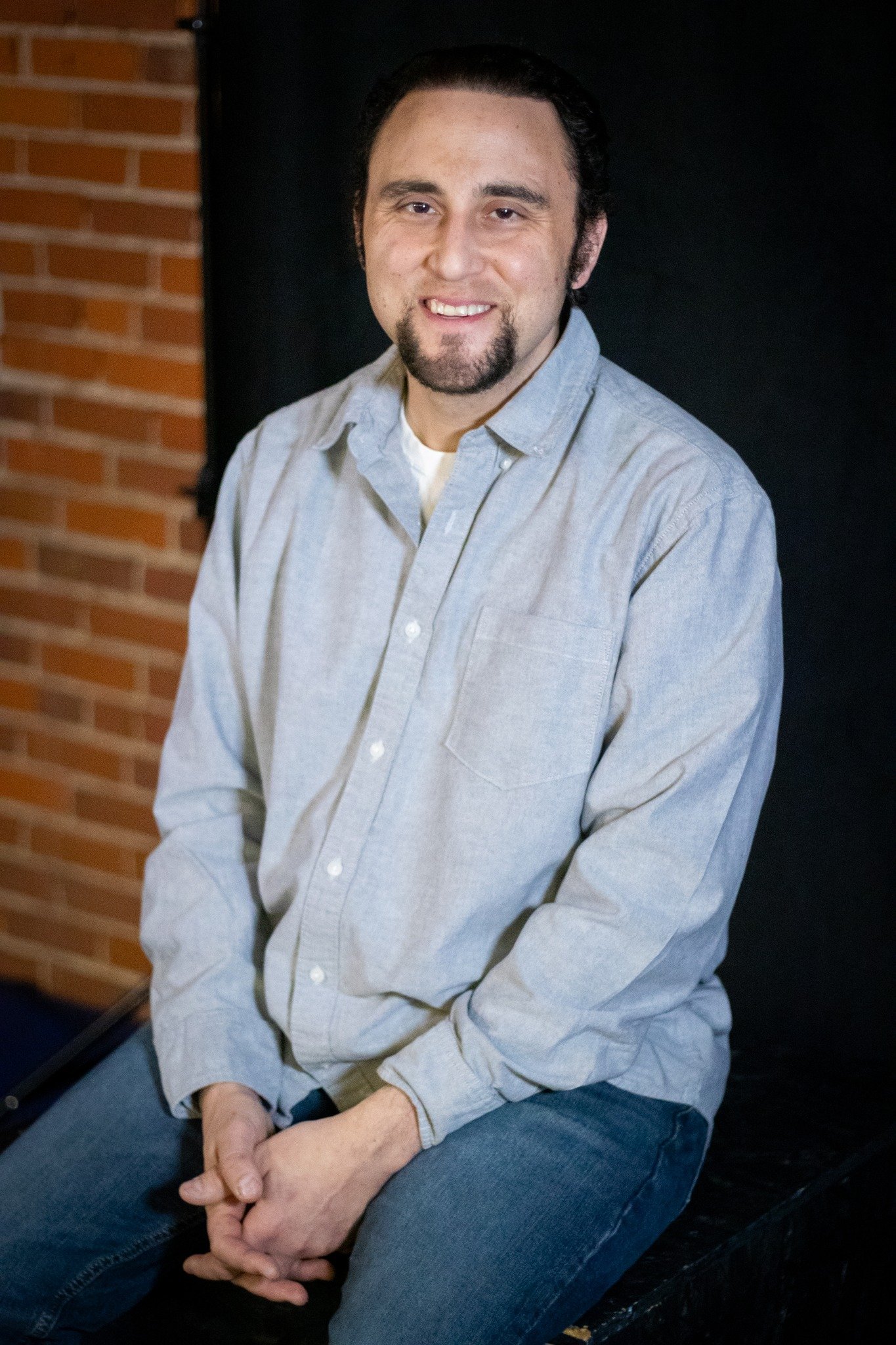 Adam Joseph Turner seated against a brick wall in a grey shirt
