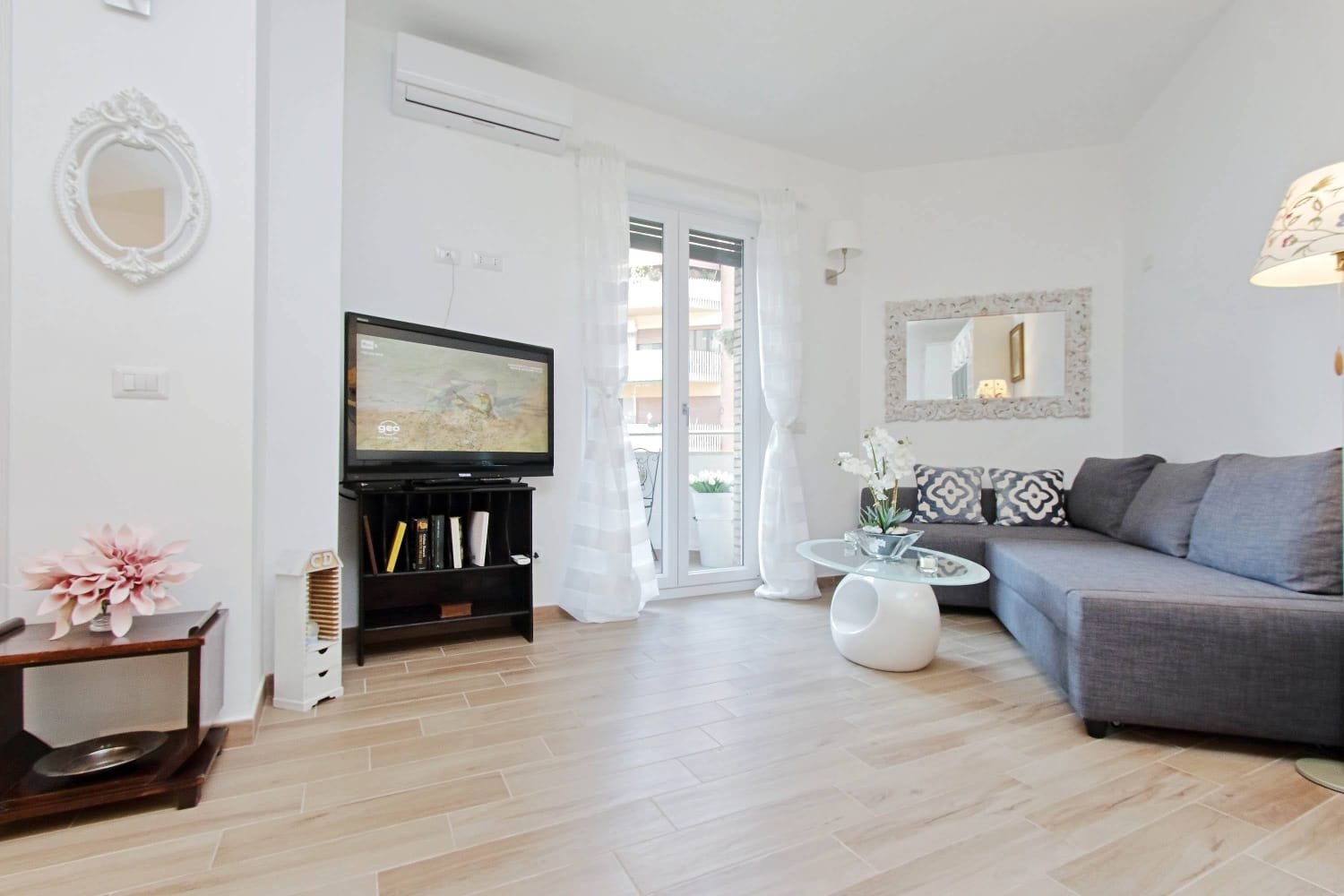 Living room with gray sofa, TV, white walls, wooden floor