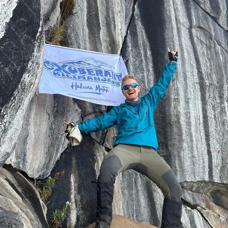 A climber celebrates with arms outstretched in front of the striped Zebra Rocks formation on Kilimanjaro.