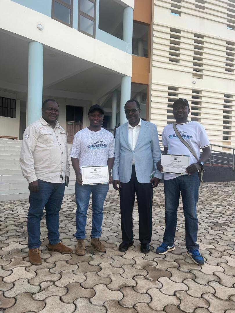 Two Exuberant team members holding certificates alongside two other people outside KCMC Hospital.