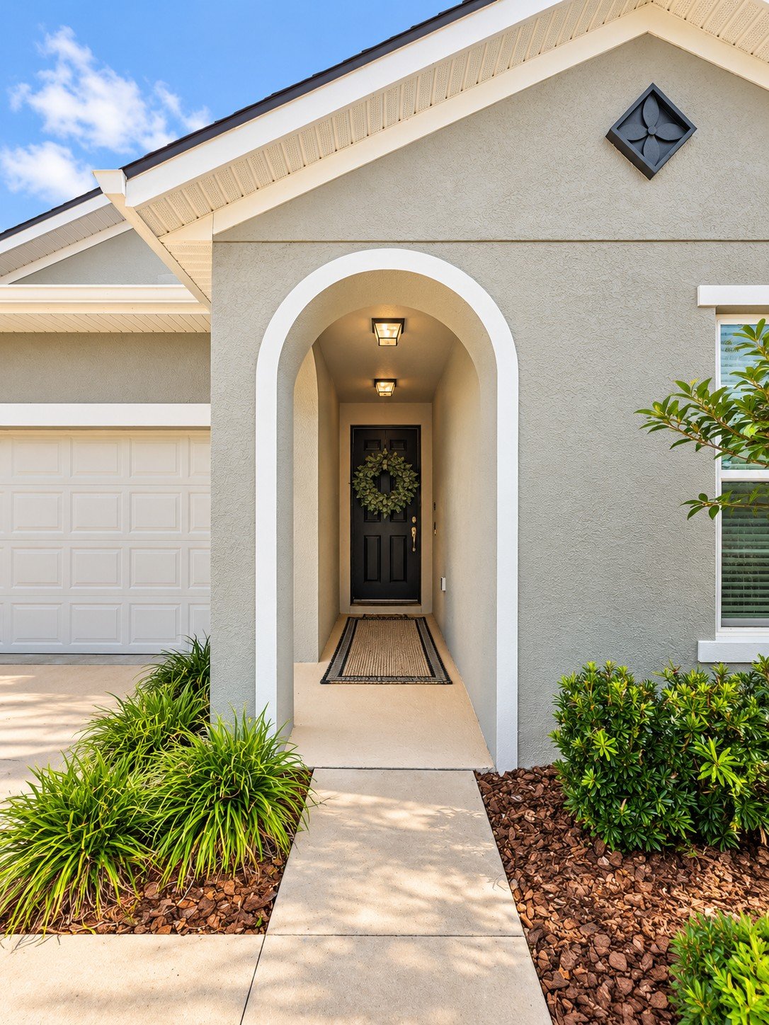 Arched covered entry with a dark front door, wreath, and landscaped walkway