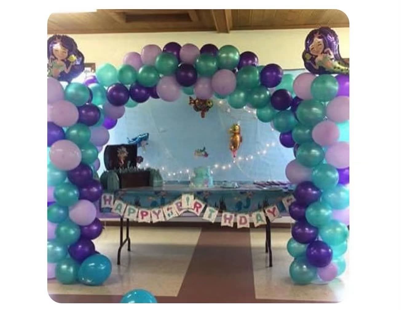 Teal and purple mermaid balloon arch framing a birthday table