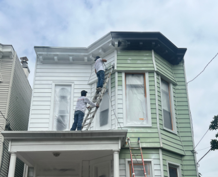 Illustrative image of professional painters working from ladders on the siding and trim of a multi-story residential home — not a specific Dumont project.