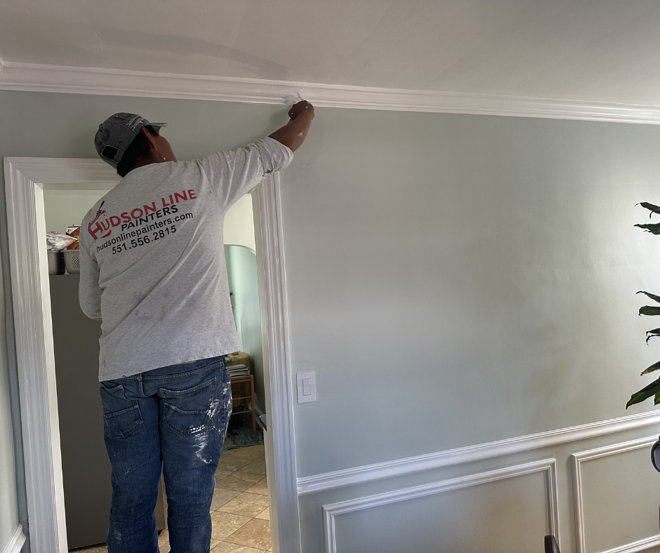 Professional painter applying finish paint along interior crown molding and wall surfaces