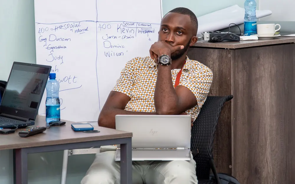 Elvis in a workshop setting with a whiteboard of team notes behind him.