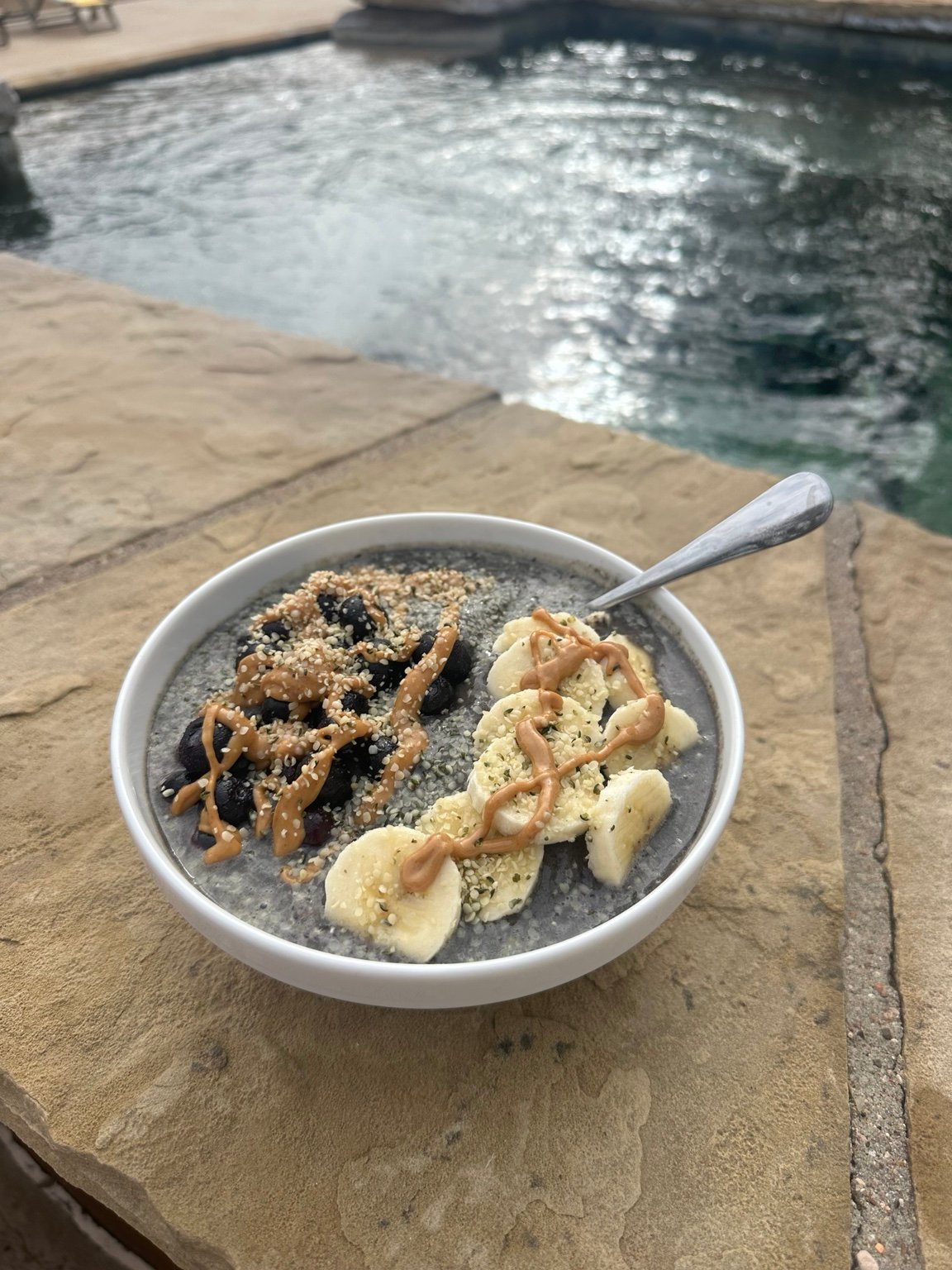 A gray smoothie bowl topped with banana, berries, seeds, and nut butter