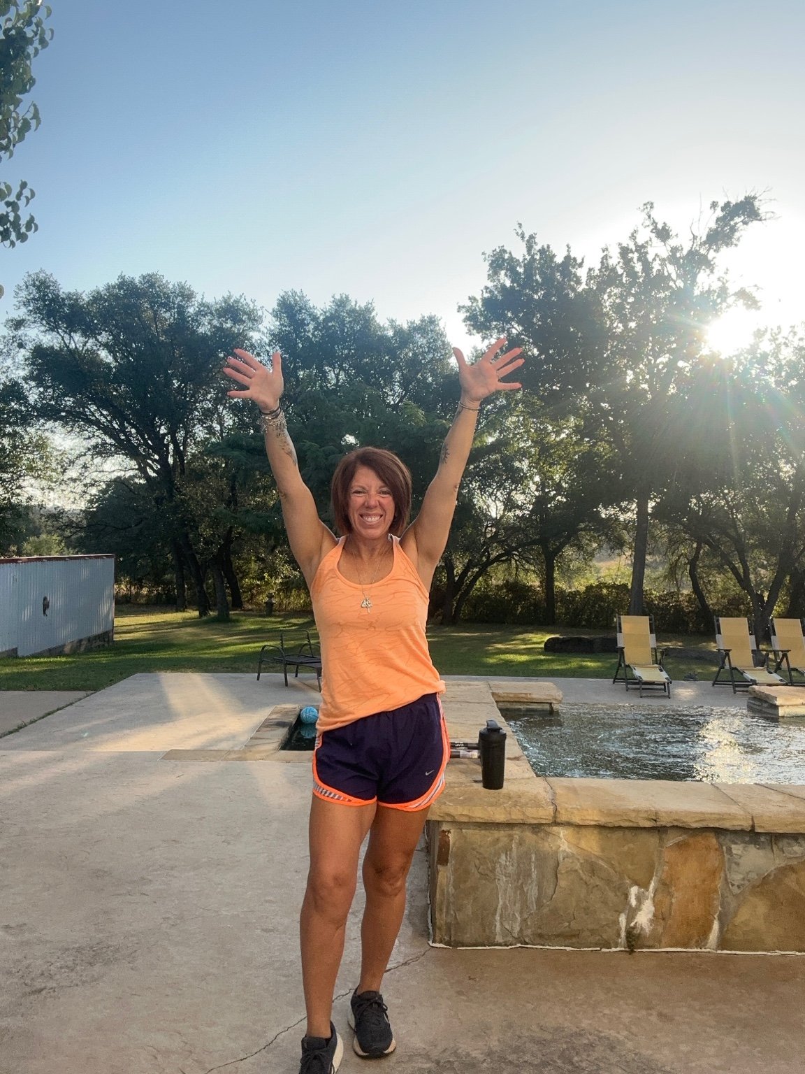 Jennifer outdoors with her arms raised