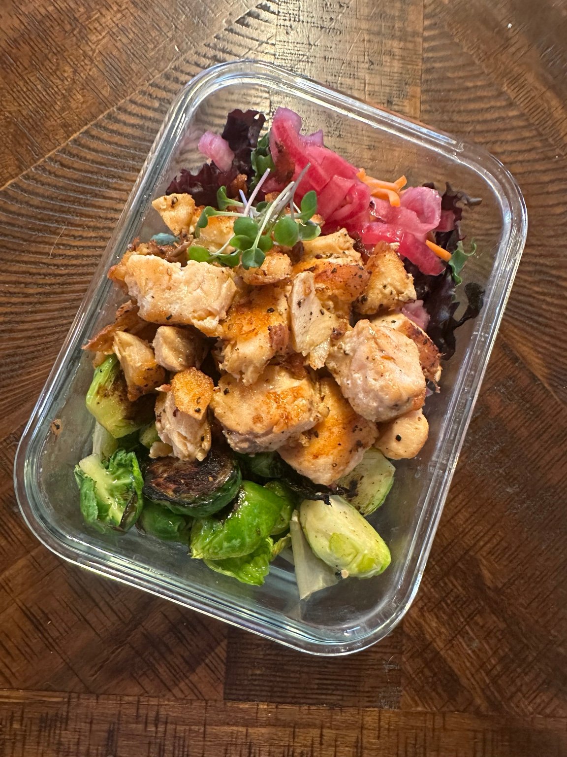 A glass container of seasoned chicken, Brussels sprouts, and pickled onions