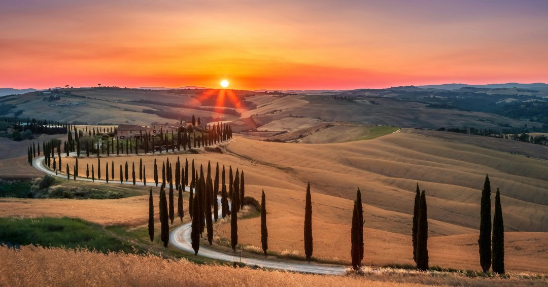 Colline della Val d'Orcia al tramonto, con un viale di cipressi che conduce a un casale