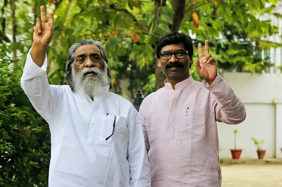 Two JMM leaders raising their hands in greeting in front of greenery