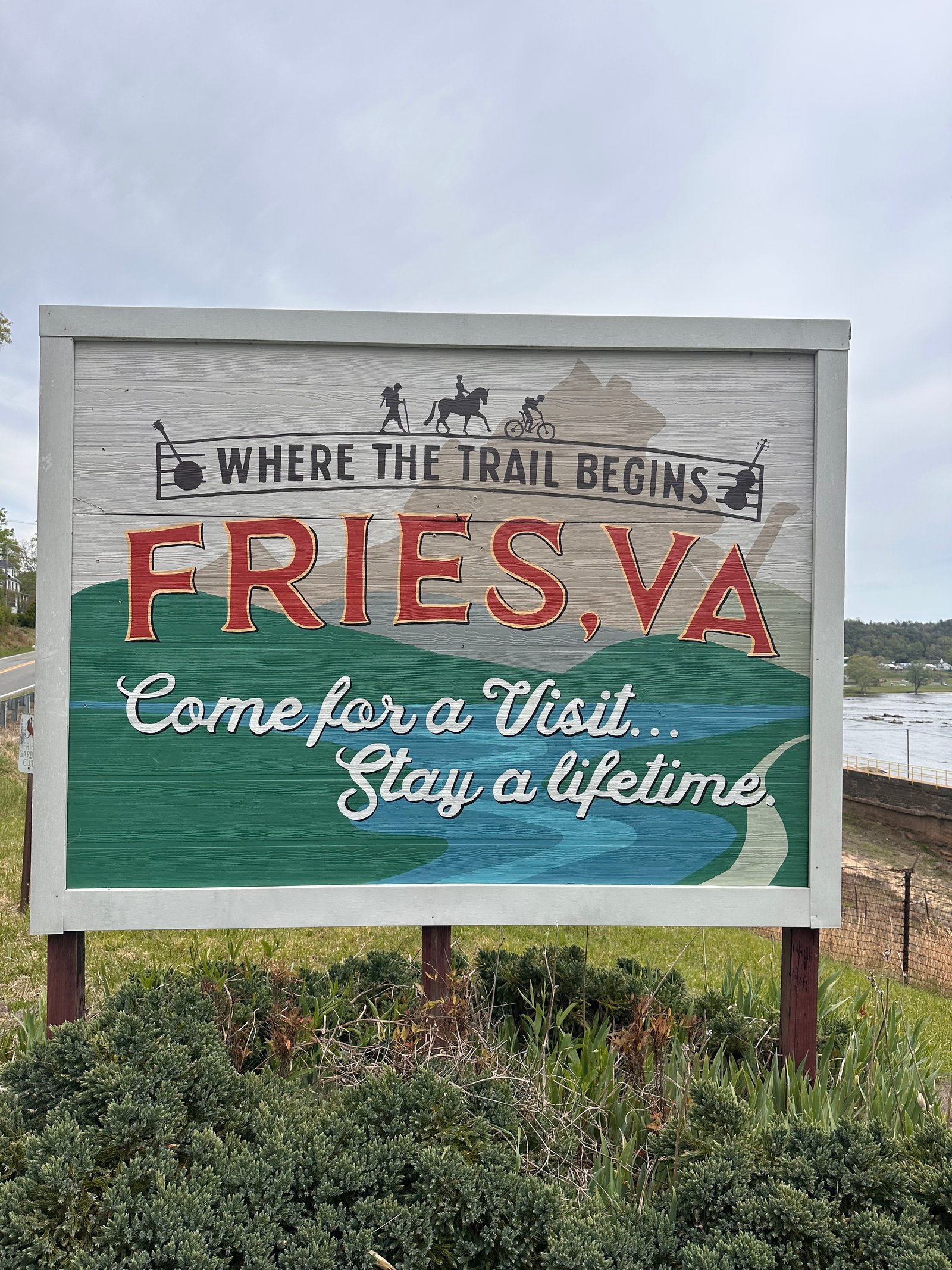 Wooden welcome sign to Fries, VA stating 'Where the Trail Begins' set against green trees