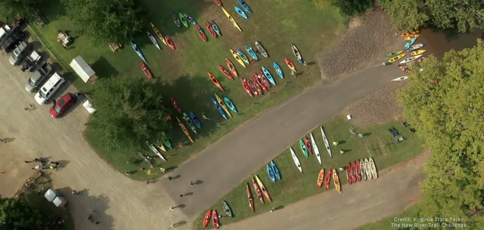Aerial view of kayak and canoe launch area with colorful boats lined up on grass and sandy beach along the New River