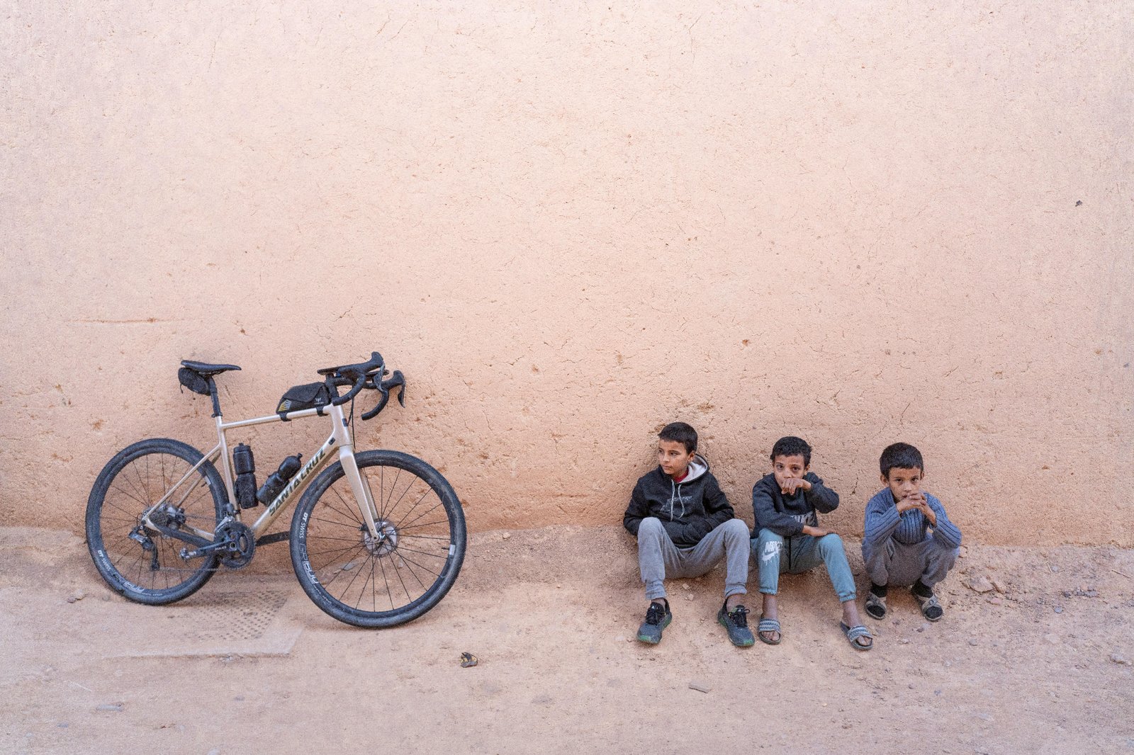 A cyclist riding a desert road as local children wave in southern Morocco