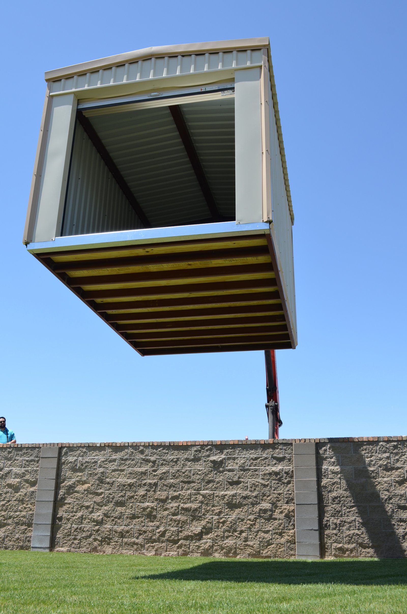 Portable storage building suspended above a wall during delivery