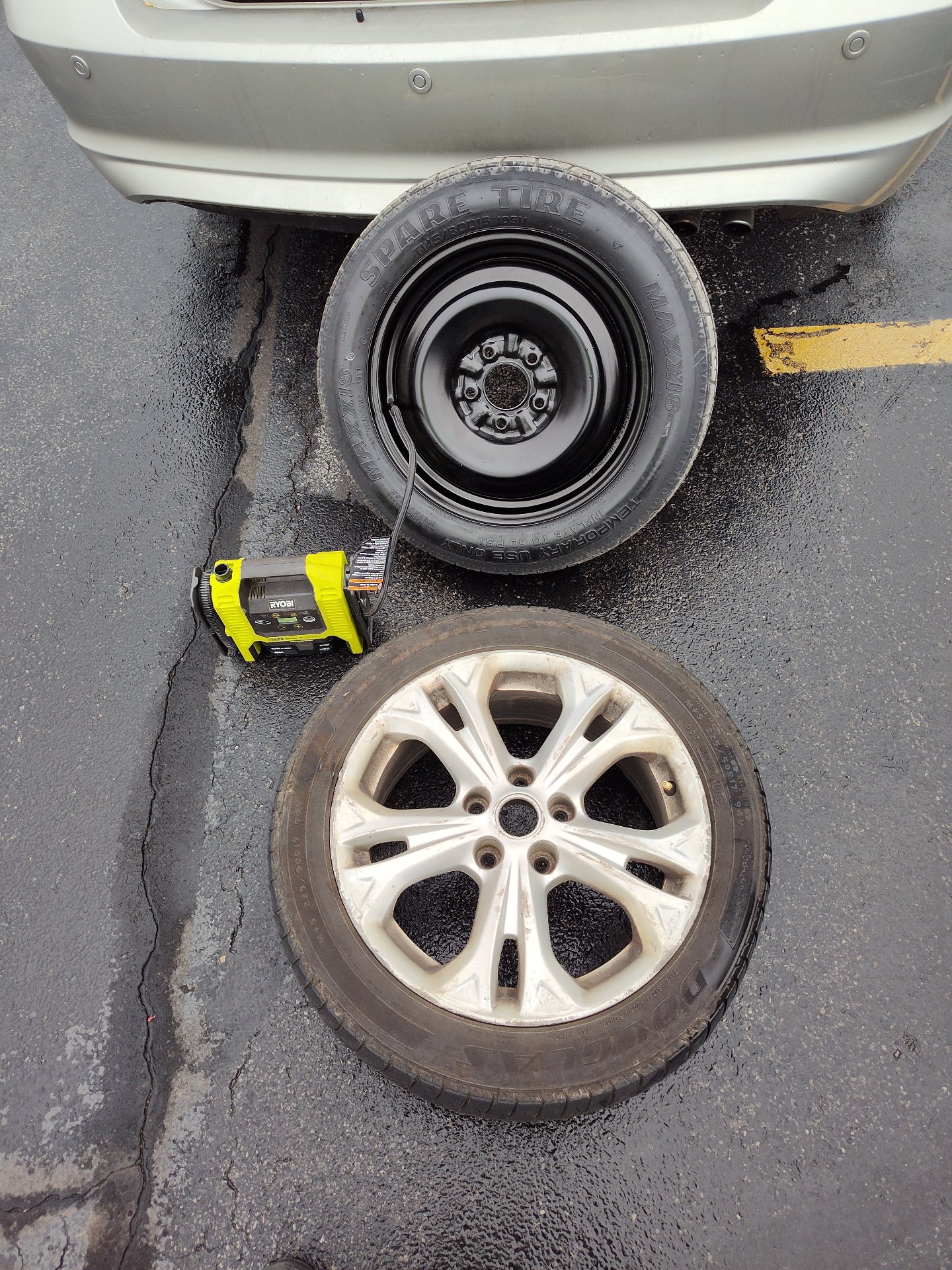 Spare tire, cordless air compressor, and flat wheel ready for a tire swap