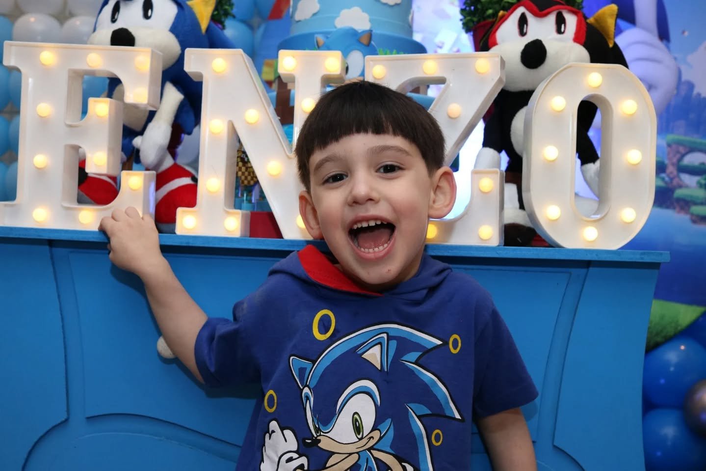 Criança feliz com letreiro "ENZO" em festa temática