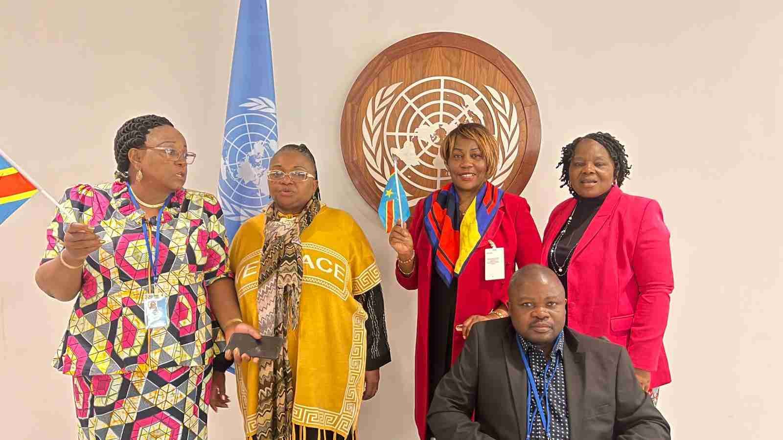 Group of people, including four women and one man, posing in front of a United Nations emblem and flag.