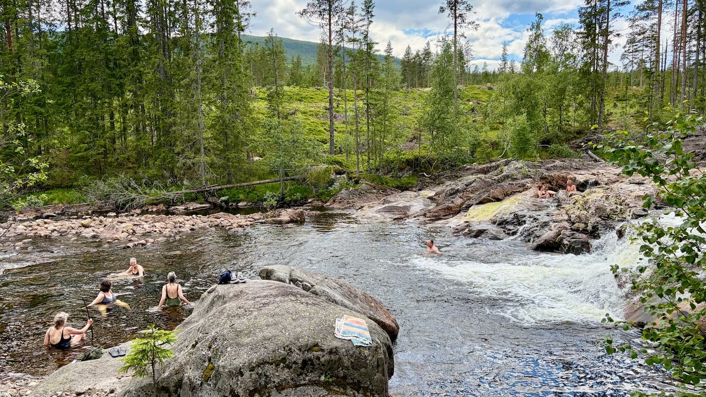 People swimming and relaxing in a natural river pool surrounded by Norwegian forest, mountains, and rocks