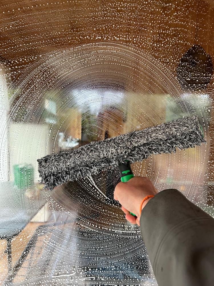 Nettoyage professionnel de vitres avec brosse microfibre et eau pure, montrant le détail du travail de nettoyage VITNET