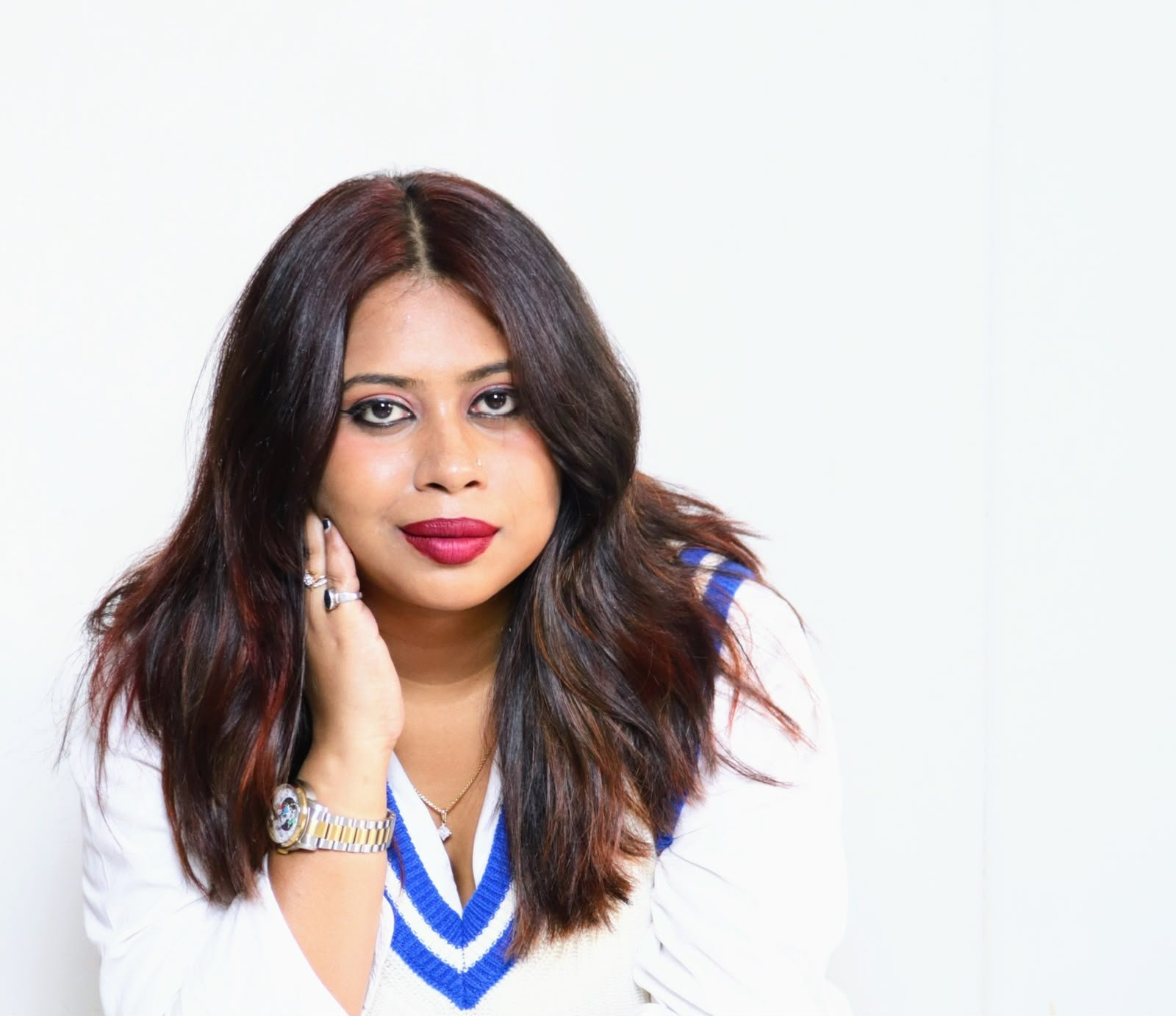 Titir Dewan, counselling psychologist, seated with one hand at her cheek, wearing a white sweater with a blue V-neck