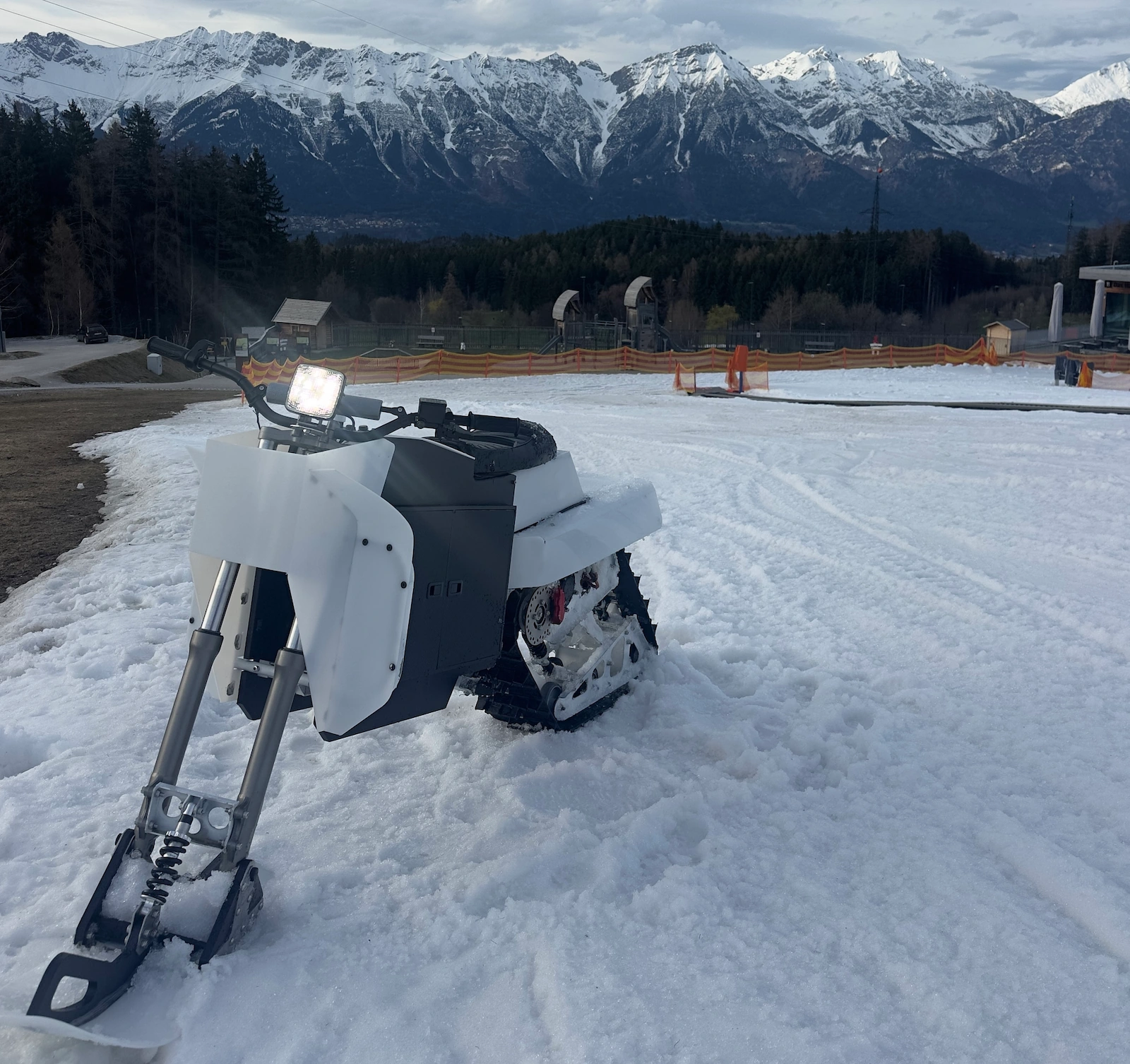 Alpsla electric snow machine parked on snow with alpine mountains in the background